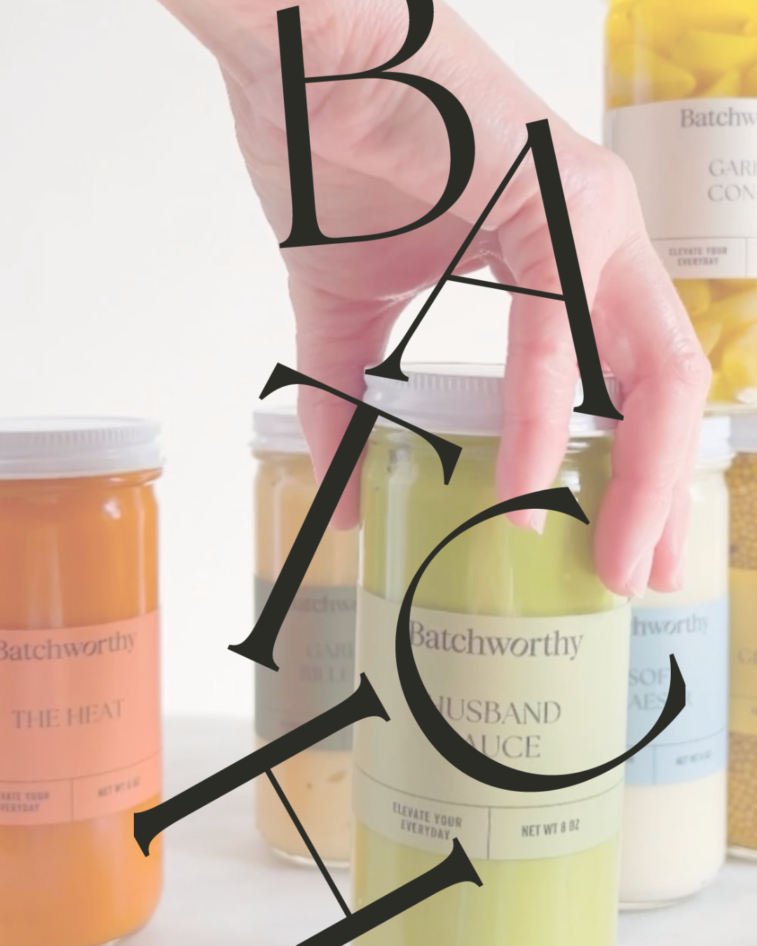 Hand holding a jar of our sauce with more sauce in the background.